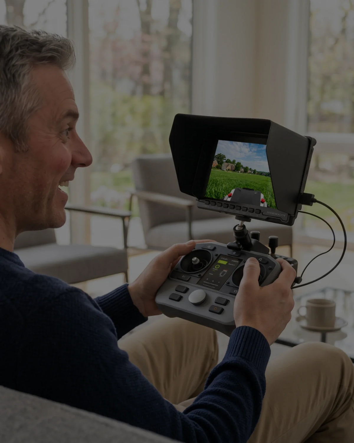 Man operating a Mowrator remote control lawn mower indoors with an FPV monitor overlooking an Australian garden