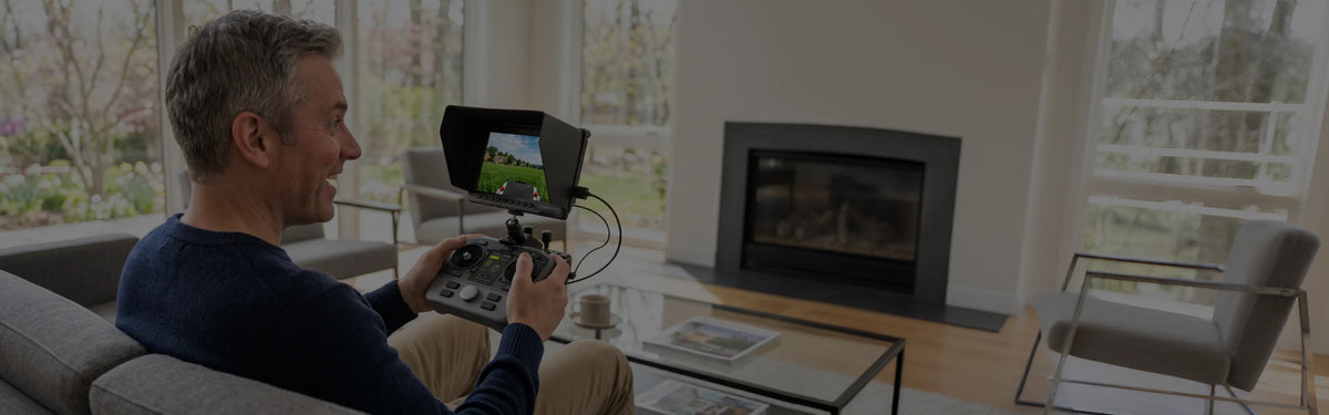 Man operating a Mowrator remote control lawn mower indoors with an FPV monitor overlooking an Australian garden